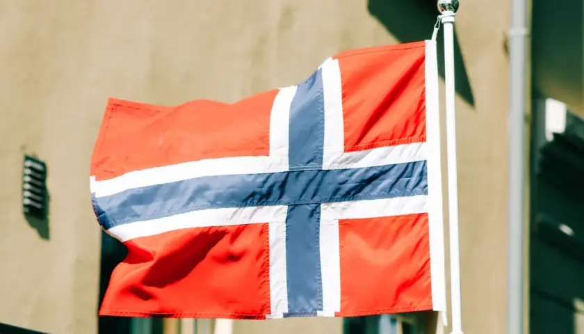 Flaga Norwegii powiewa na maszcie na tle budynku.