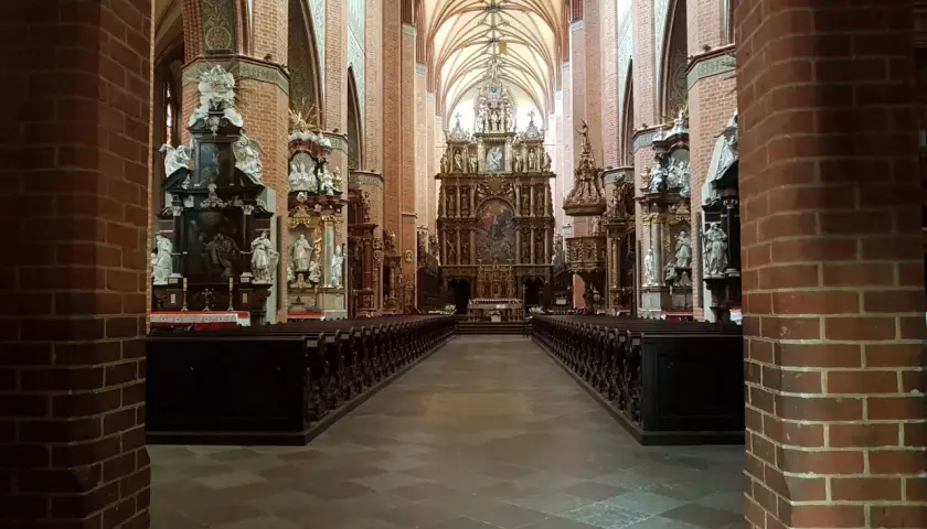 Wnętrze katedry w Pelplinie z rzędami ławek i bogato zdobionym ołtarzem głównym.