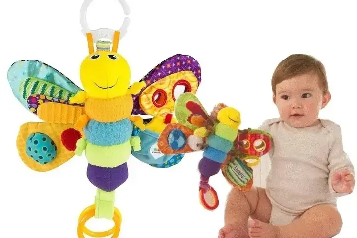 Kolorowy motylek Lamaze z grzechotką i piszczałką, obok siedzącego niemowlaka.