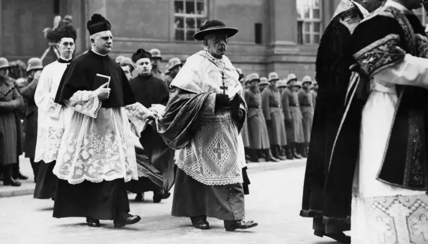 Geistliche in feierlicher Kleidung marschieren, im Hintergrund Soldaten. Die Kirchensteuer im Nationalsozialismus war ein komplexes Thema.