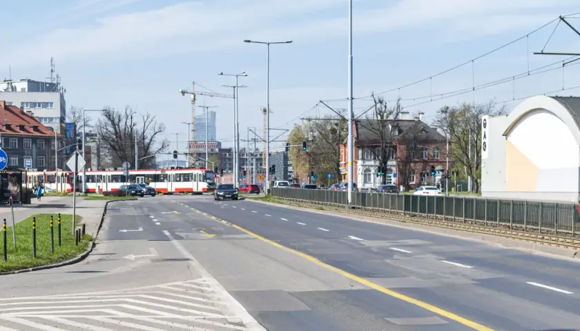 Ulica z tramwajem, samochodami i budynkami w tle.