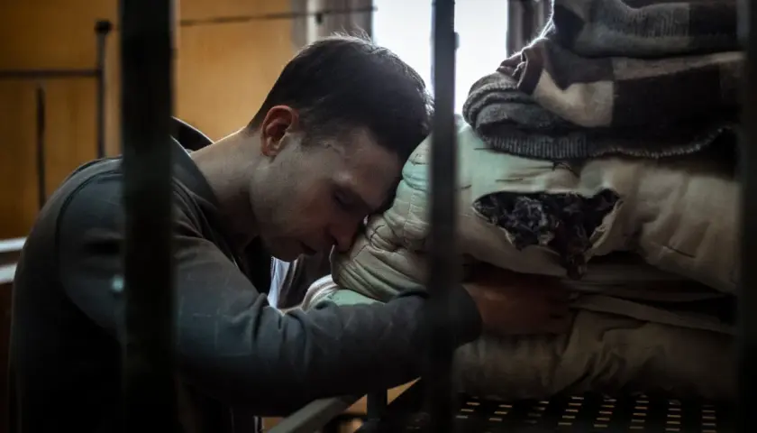 Młody mężczyzna opiera głowę na poduszce w celi. Scena z filmu o Tomaszu Komendzie, ukazująca jego trudne chwile.