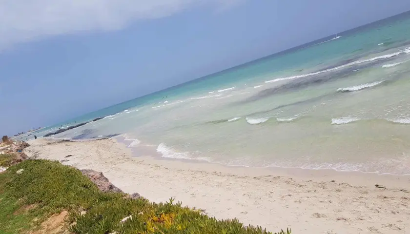 Piękne djerba plaże z turkusową wodą i białym piaskiem. W oddali widać kilka osób kąpiących się w morzu.
