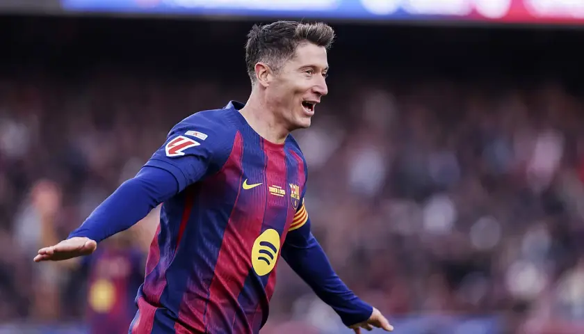 Piłkarz Robert Lewandowski w koszulce FC Barcelony świętuje bramkę na tle trybun.