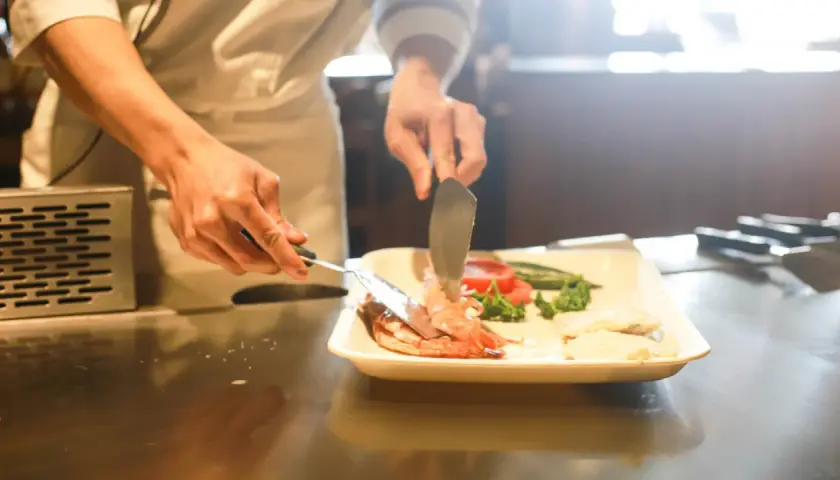 Kucharz przygotowuje danie z krewetek i warzyw, ćwicząc umiejętności do egzaminu zawodowego gastronomia.