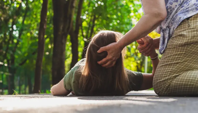 Osoba na ziemi, być może doświadczająca nietypowych objawów padaczki, otrzymuje pomoc od drugiej osoby.