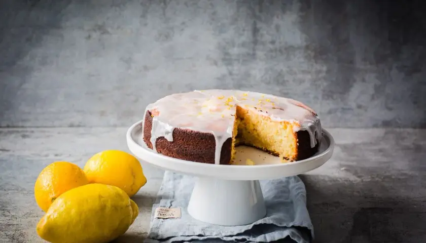 Ein saftiger zitronenkuchen mit Zuckerguss und Zitronenschale, daneben frische Zitronen.