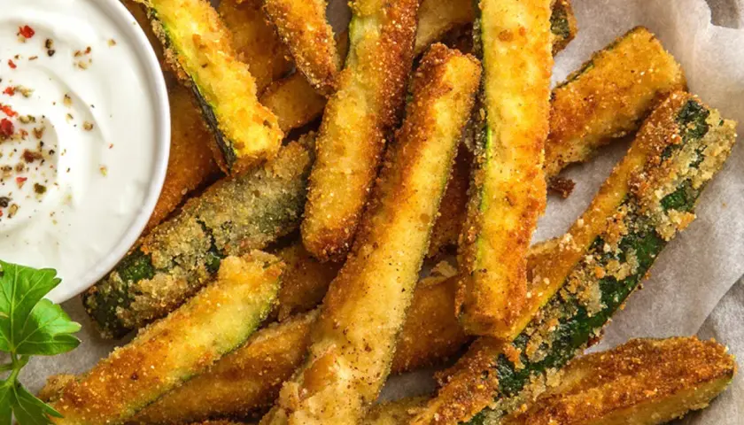Bastoncini croccanti di zucchine in friggitrice ad aria, dorati e invitanti, serviti con una salsa cremosa.