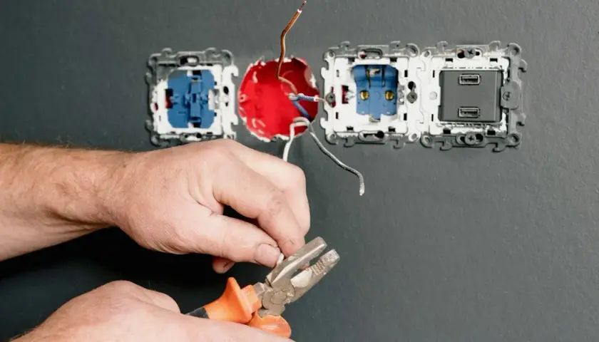Ręce elektryka z kombinerkami przygotowują przewody do podłączenia do gniazdka.