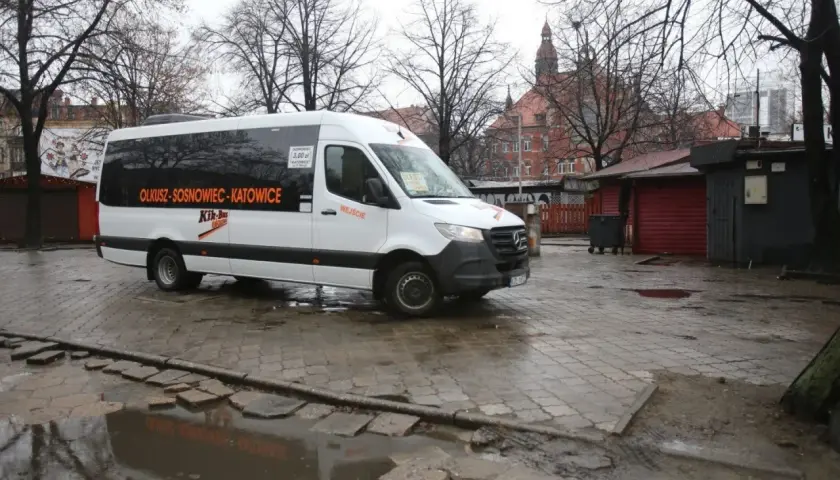 Biały bus Kik-Bus z napisem "OLKUSZ-SOSNOWIEC-KATOWICE" na mokrym placu przed budynkiem dworca.