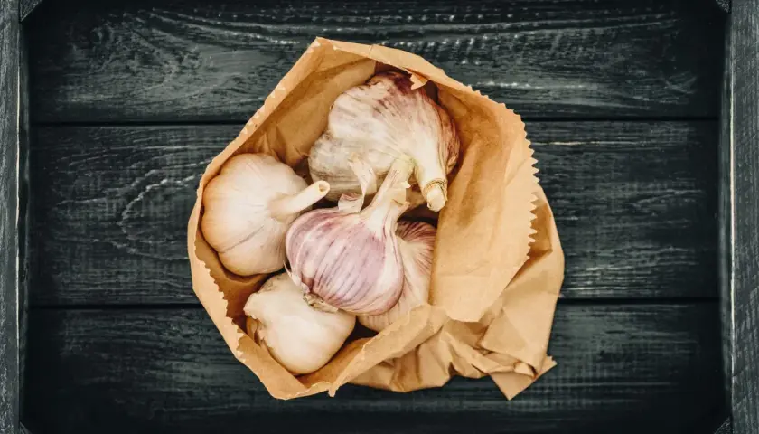 Frische Knoblauchzehen in einer Papiertüte, bereit zum **knoblauch lagern** auf dunklem Holz.