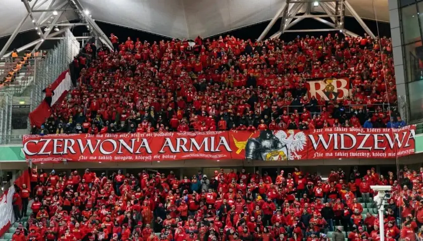 Tłum kibiców Widzewa w czerwonych barwach, z transparentem "Czerwona Armia Widzewa".