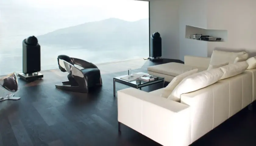 Modernes Wohnzimmer mit Panoramafenster, das eine atemberaubende Aussicht bietet. Ein weißes Ledersofa, ein futuristischer Sessel und zwei schlanke Lautsprecher ergänzen die minimalistische Einrichtung. Das Panoramafenster dekorieren wir hier mit der N...