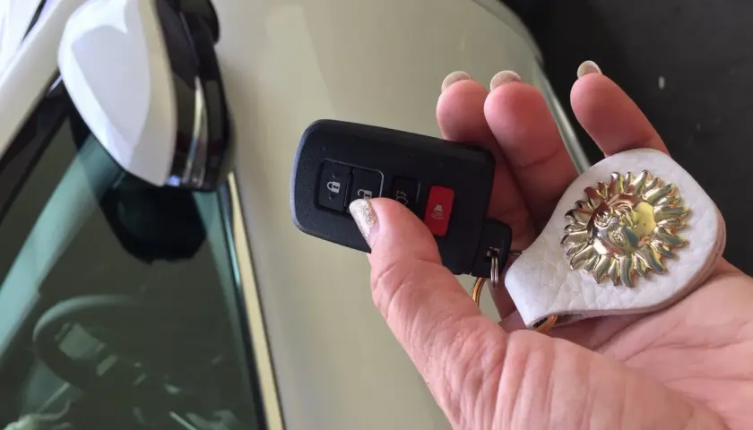 Uszkodzony transponder w kluczyku objawy: auto nie odpala, miga kontrolka. Dłoń trzyma kluczyk z breloczkiem w kształcie słońca.