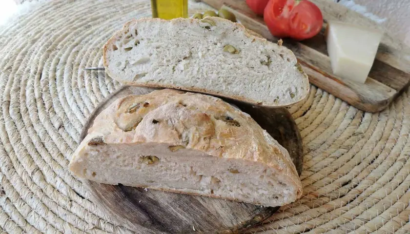 Pan rústico con aceitunas, tomates, queso y aceite de oliva. Un delicioso pan de aceitunas listo para disfrutar.