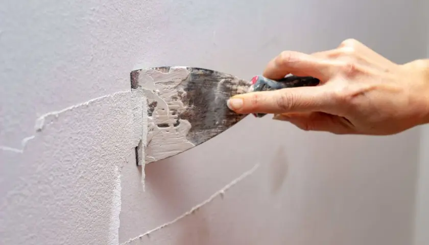 Mano usa una spatola per rimuovere la pittura lavabile dal muro, un passo fondamentale per preparare la parete a una nuova tinteggiatura.