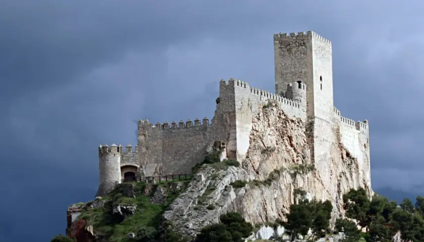 Castillo medieval en lo alto de un peñasco, parte de la ruta de la lana, bajo un cielo tormentoso.
