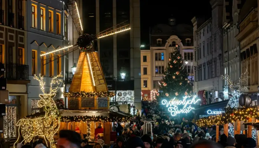 Tłum ludzi na jarmarku bożonarodzeniowym w Kujawsko-Pomorskiem. Świecący renifer, drewniany wiatrak i choinka tworzą magiczną atmosferę.