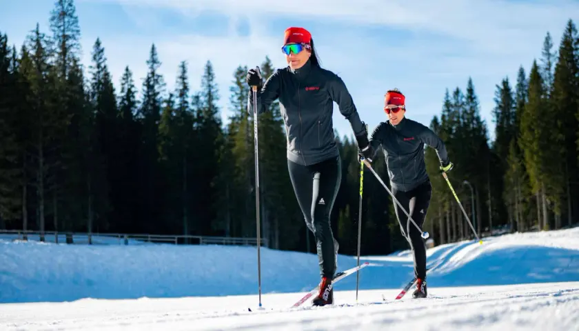 Dwie kobiety w sportowych strojach pokonują trasę narciarską. Długość nart biegowych jest kluczowa dla ich szybkości i stabilności na śniegu.