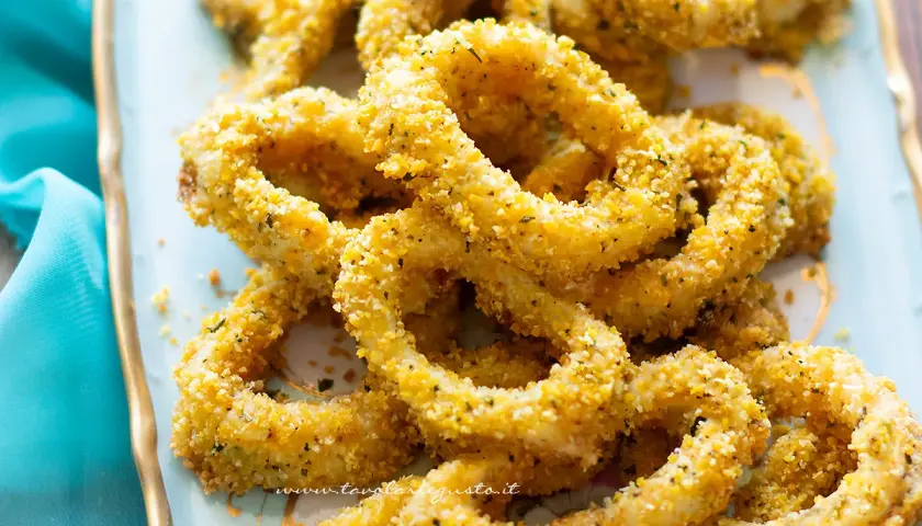 Anelli di totano al forno dorati e croccanti, serviti su un piatto azzurro con un tovagliolo blu.