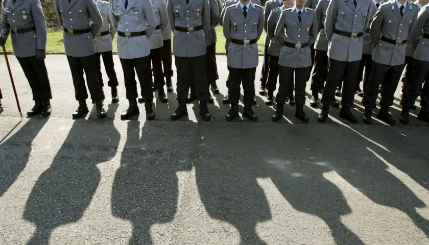 Soldaten der Bundeswehr in Uniform mit grünen Baretts stehen Spalier. Ihre Schatten werfen lange Linien auf den Asphalt.