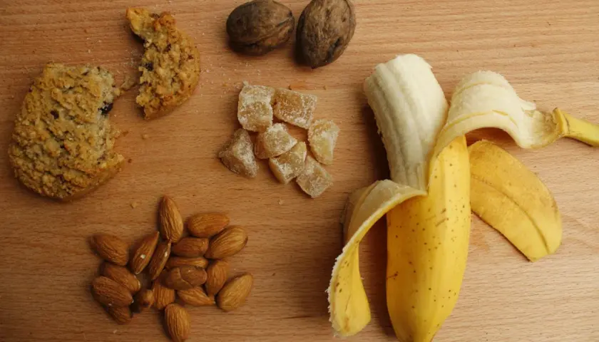 Ciastko, banan, migdały i kandyzowany imbir – wszystko, co ma dużo węglowodanów, na drewnianym blacie.