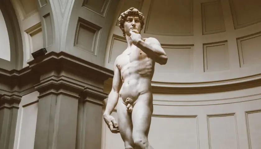 Michelangelo's David statue, a marble sculpture of a nude male figure, stands in a grand hall.