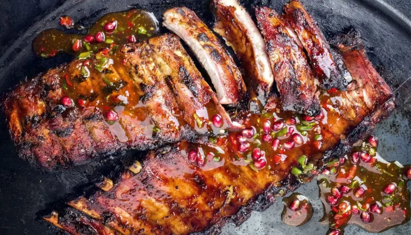 Soczyste żeberka w marynacie, polane aromatycznym sosem z granatem i chili, podane na metalowej tacy.