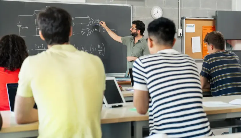 Nauczyciel tłumaczy schemat na tablicy, studenci słuchają. To część jego pensum, by przekazać wiedzę.