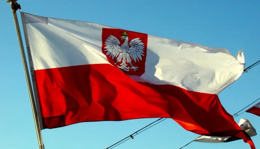 Polska flaga na statku powiewa na wietrze na tle błękitnego nieba. Biało-czerwona flaga z orłem w koronie dumnie reprezentuje kraj.
