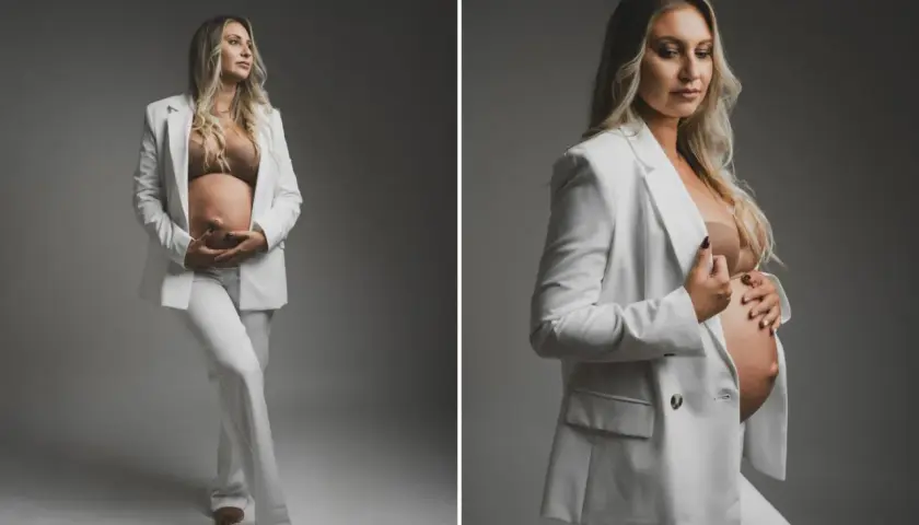 Elegancka sesja ciążowa w studio. Przyszła mama w białym garniturze czule obejmuje brzuszek.