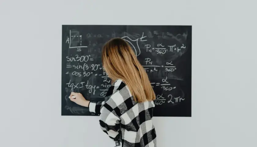 Dziewczyna w kratkę pisze wzór na tablicy. Wzór na t to skomplikowane równanie matematyczne.