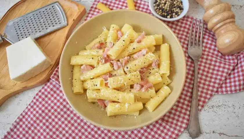 Pyszne pasta alla gricia z guanciale i pecorino, posypana świeżo mielonym pieprzem. Obok ser, tarka i młynek do pieprzu.