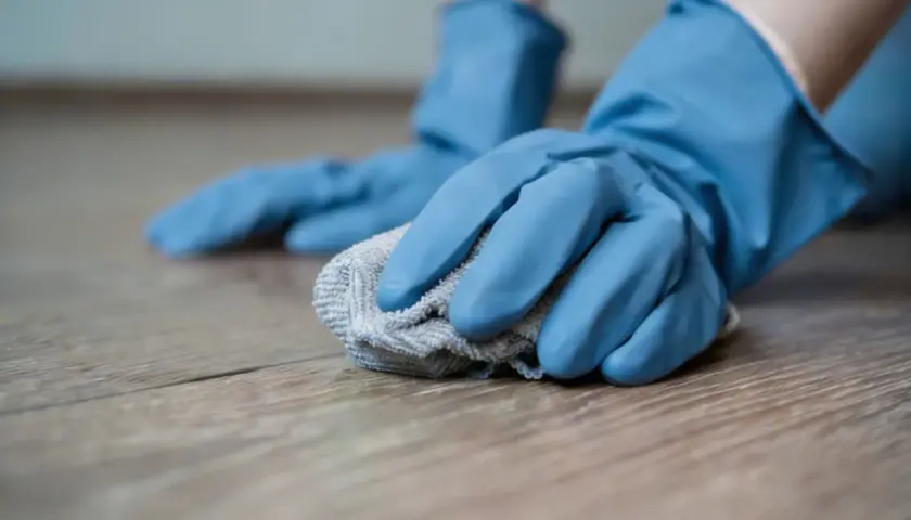 Mani con guanti blu puliscono un pavimento in gres porcellanato opaco con un panno grigio.