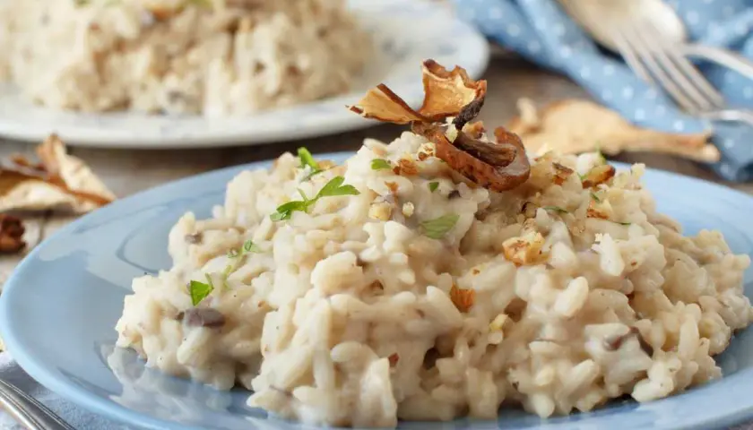 Delicioso risotto de setas cremoso, adornado con trozos de champiñones secos y nueces picadas, servido en un plato azul.