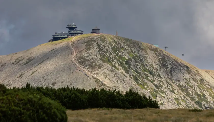 Schronisko i obserwatorium na szczycie w Karkonoszach, z widoczną kolejką linową i kamienistym zboczem.
