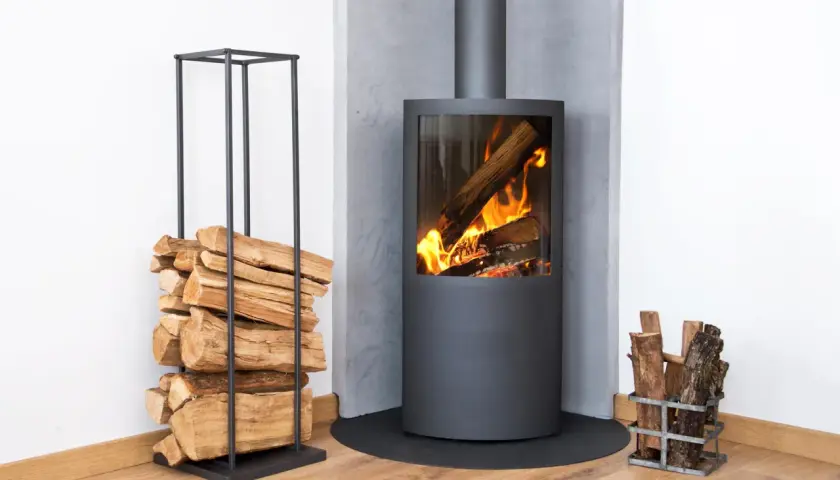 Moderner Kamin mit brennendem Holz. Ein Stapel Holz daneben. Diskussionen über ein holzheizung verbot sind angesichts dieser gemütlichen Szene unwahrscheinlich.