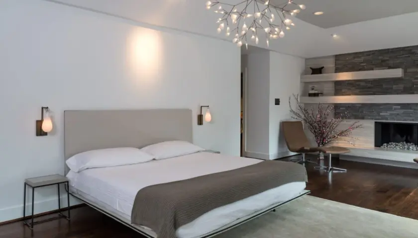 Camera da letto moderna con letto king-size, camino in pietra e un'elegante controsoffittatura che valorizza il design.