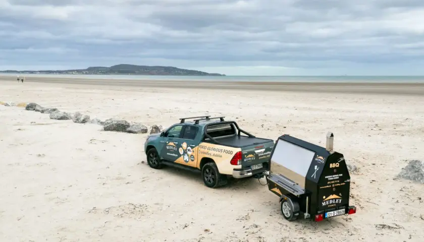 Un pick-up tracte un barbecue sur remorque sur une plage. Idéal pour fabriquer un barbecue sur remorque pour un événement en bord de mer.
