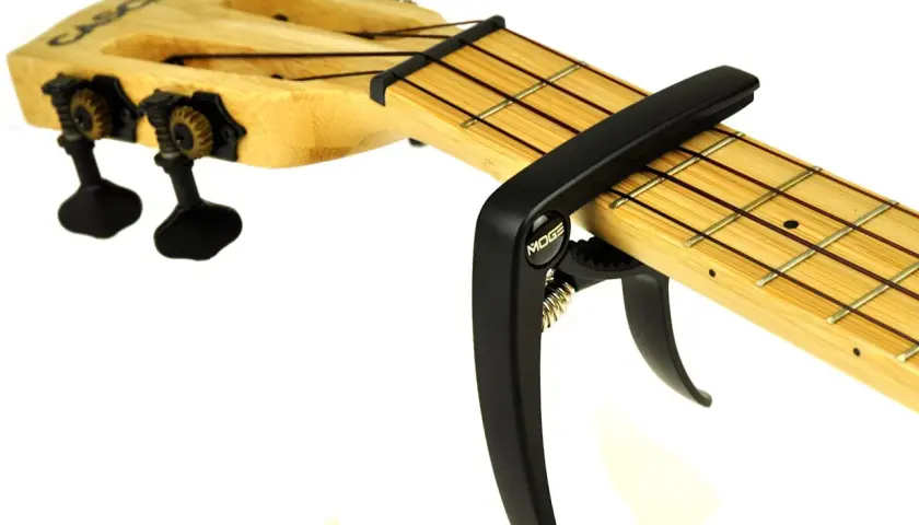 Czarny kapodaster do ukulele marki Moge na drewnianej podstrunnicy z widocznymi progami i strunami.