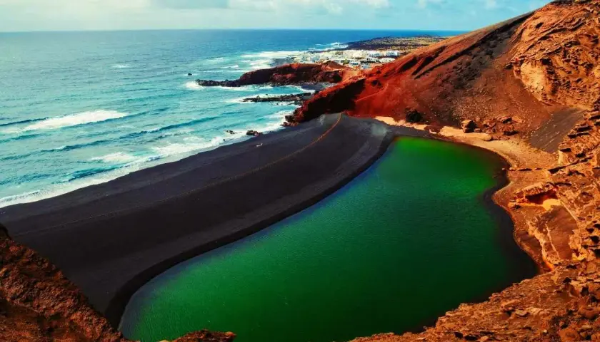 Zielona laguna otoczona czarną plażą i czerwonymi skałami. Niezwykłe miejsce, które warto zobaczyć na Lanzarote.
