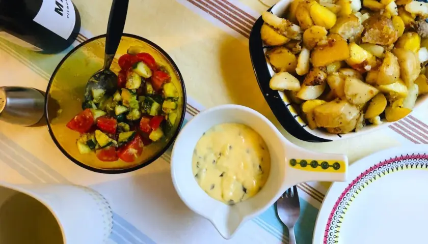 En skål med bearnaisesås recept, bredvid en sallad med tomat och gurka samt ugnsrostade potatisar.