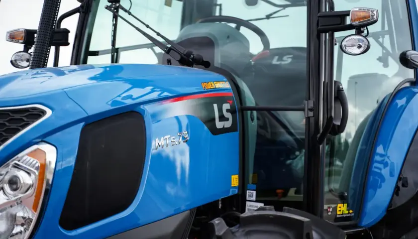 Niebieski ciągnik LS MT5.73 z napisem "POWER SHUTTLE" na błotniku. W kabinie widoczna kierownica i siedzenie.