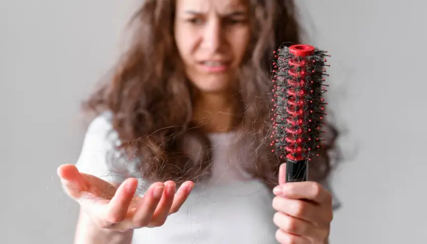 Mujer preocupada muestra mechones de pelo en su mano y un cepillo con más cabello, buscando un tratamiento para pelo que se rompe.