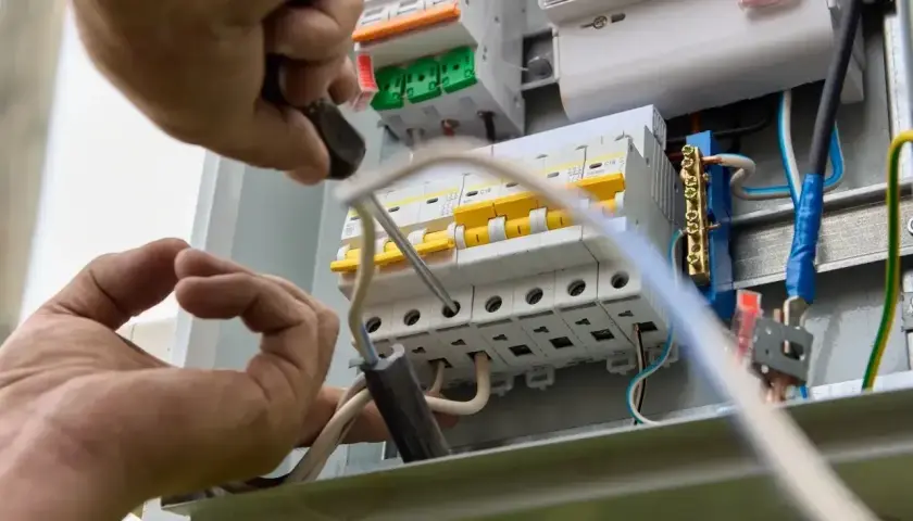 Elektryk montuje bezpieczniki w skrzynce, dobierając odpowiednie jakie bezpieczniki do mieszkania w bloku.