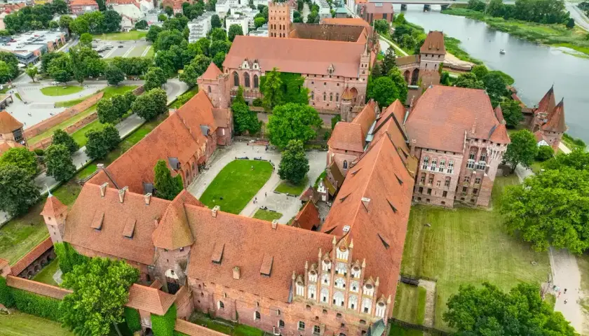 Potężny zamek w Malborku, z czerwonymi dachami i zielonymi dziedzińcami, rozciąga się wzdłuż rzeki Nogat.