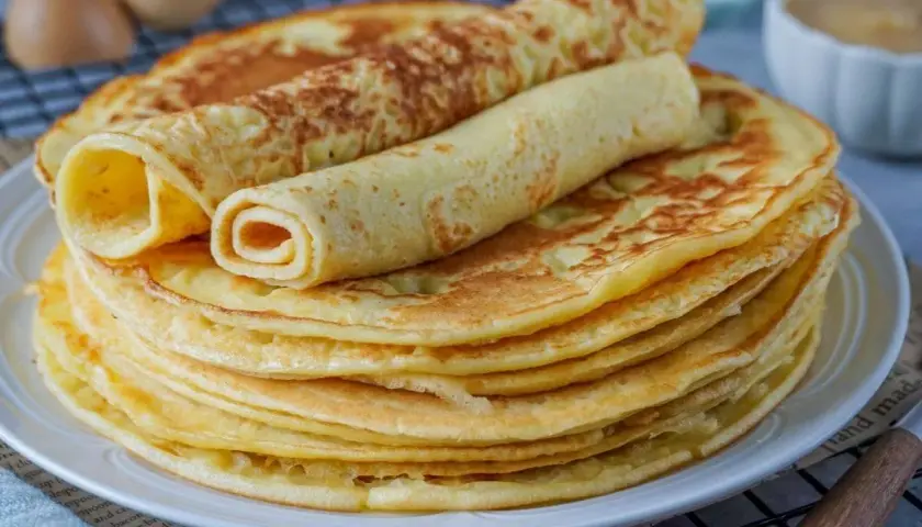 Ein Stapel goldbrauner Eierkuchen, zwei davon gerollt, warten auf ein leckeres Eierkuchen Rezept.