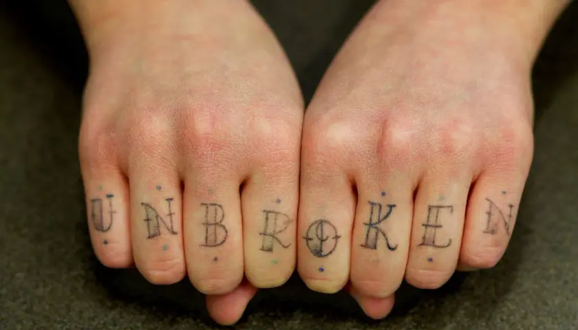 Tatuaż na palcach tworzy napis "UNBROKEN". To jak trwały pierścionek, symbol siły.