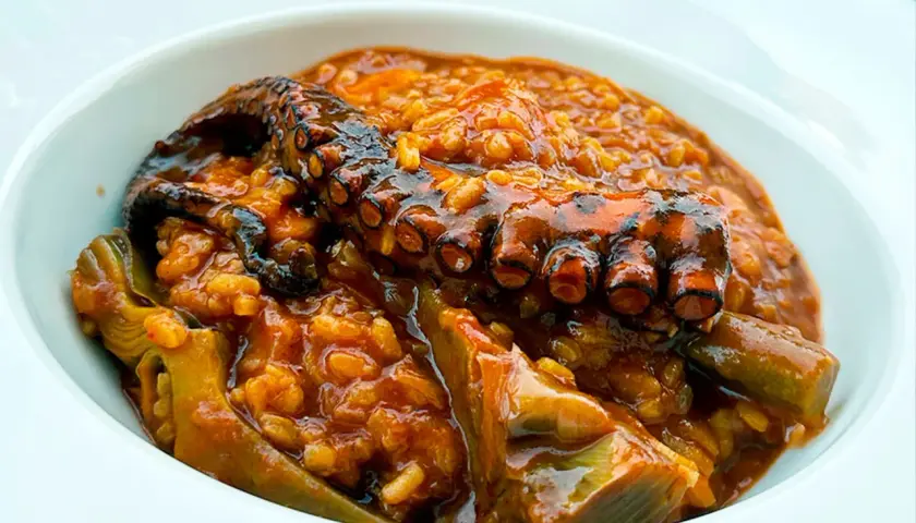 Delicioso arroz con pulpo y trozos de alcachofa en un cuenco blanco.