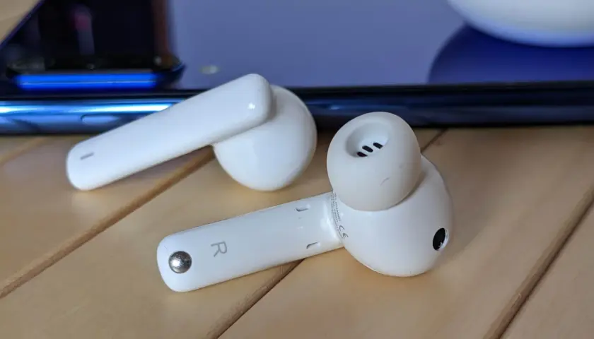Białe słuchawki Huawei leżą obok niebieskiego smartfona. Dowiedz się, jak podłączyć bezprzewodowe słuchawki Huawei.